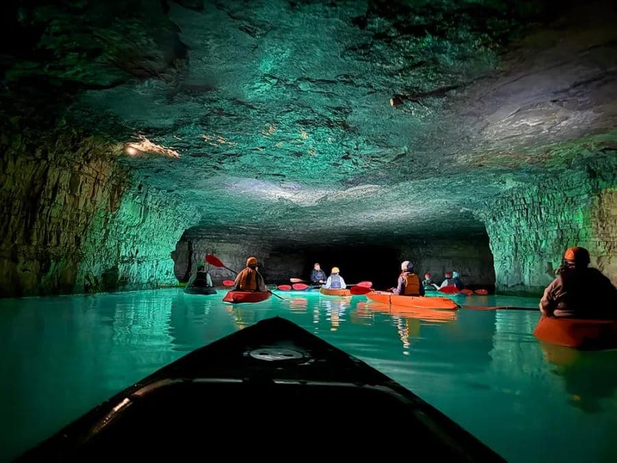 Kayakers paddling through a flooded underground cavern lit in turquoise